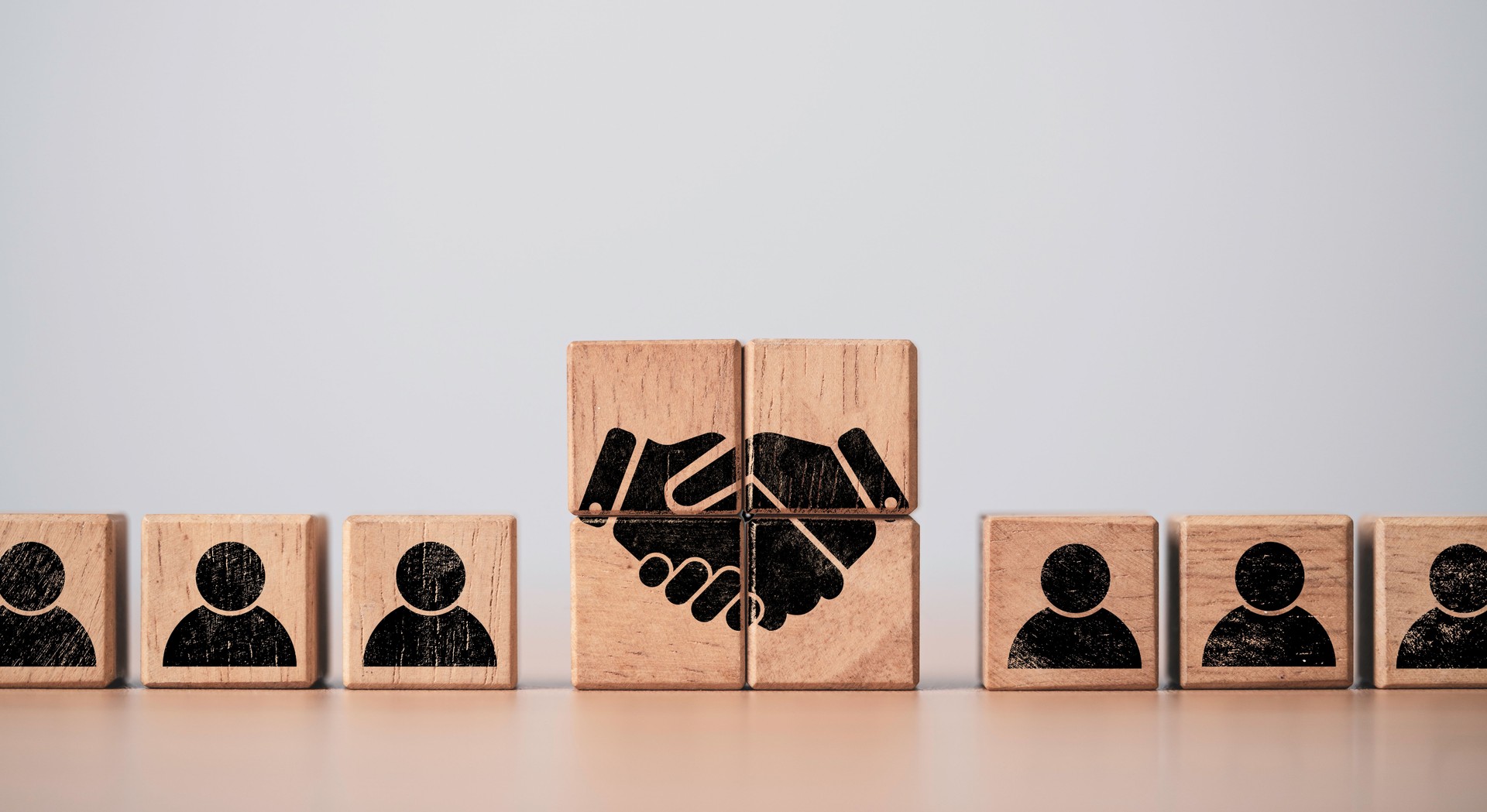Hand shaking print screen on wooden block cube between human icon for business deal and agreement concept.